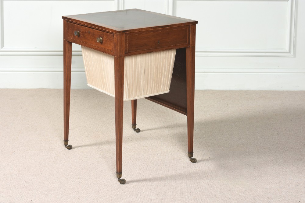 An 18th-century Sheraton rosewood sewing table featuring a top drawer, a suspended cream pleated fabric work bag, square tapered legs, and brass castors.