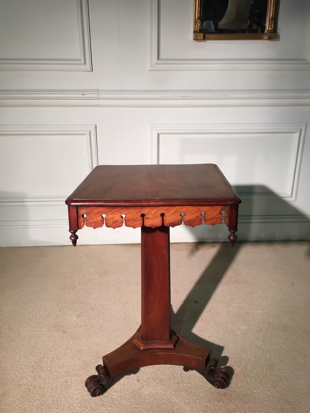 A 19th-century William IV mahogany occasional table featuring a square top, decorative pierced apron with drop finials, central column support, and a triform base on scroll feet.