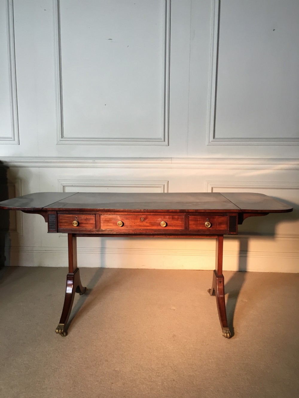 A Georgian mahogany sofa table with two drop leaves, front drawers with brass knobs, and splayed legs ending in brass claw castors. View II