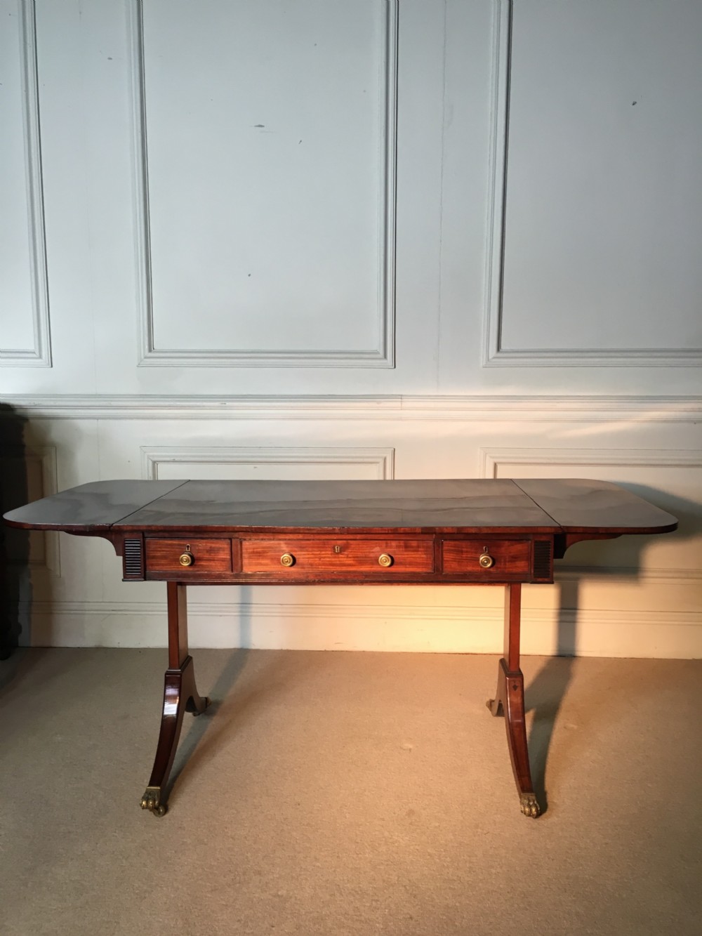 A Georgian mahogany sofa table with two drop leaves, front drawers with brass knobs, and splayed legs ending in brass claw castors. View V
