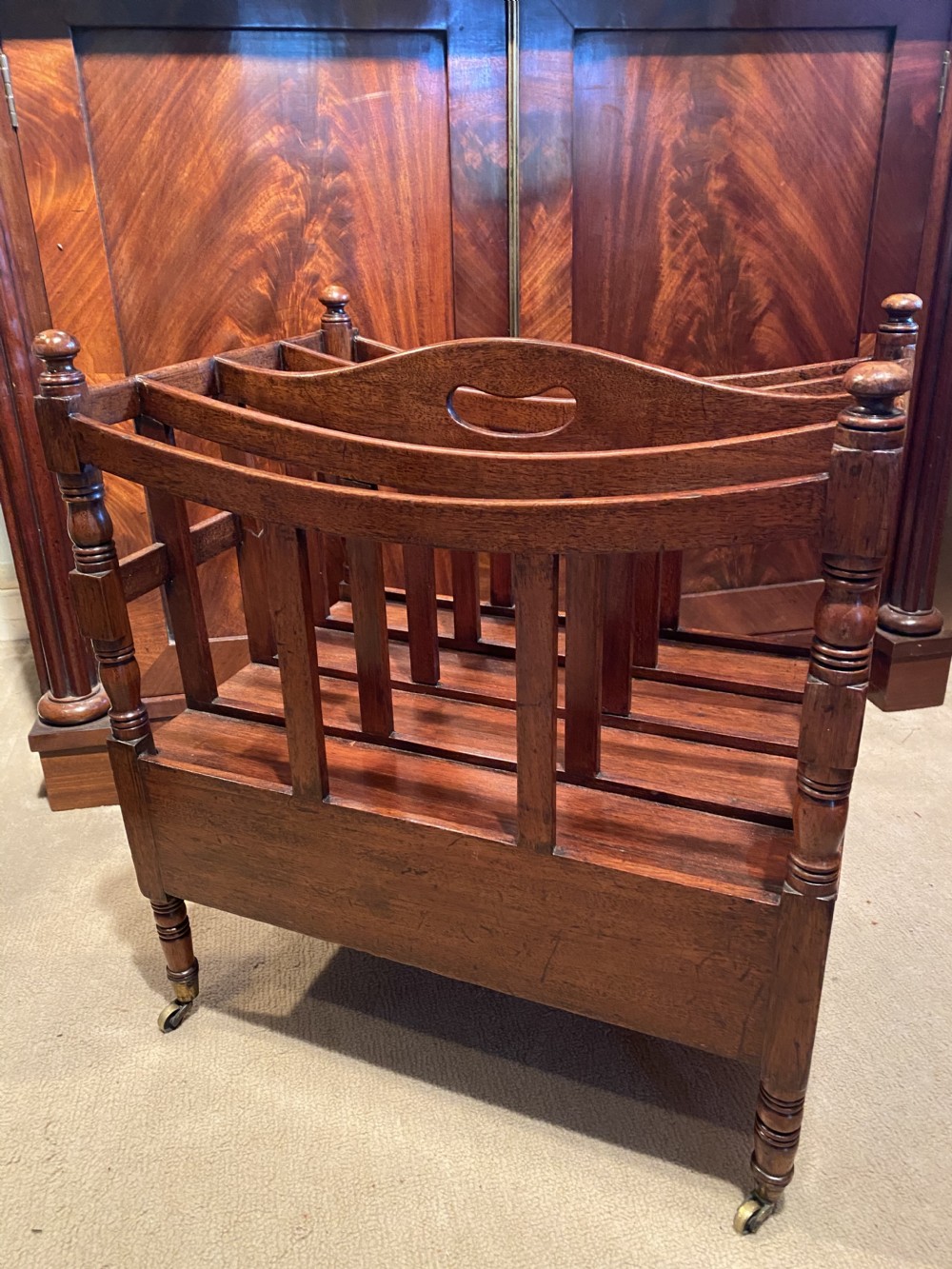 A George III mahogany canterbury featuring four slatted compartments, a single base drawer with brass knobs, and turned legs with brass castors. View V