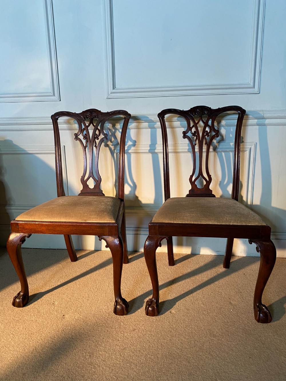A pair of 19th-century Chippendale style dark mahogany dining chairs featuring carved pierced back splats, upholstered seats, and cabriole front legs ending in ball and claw feet.