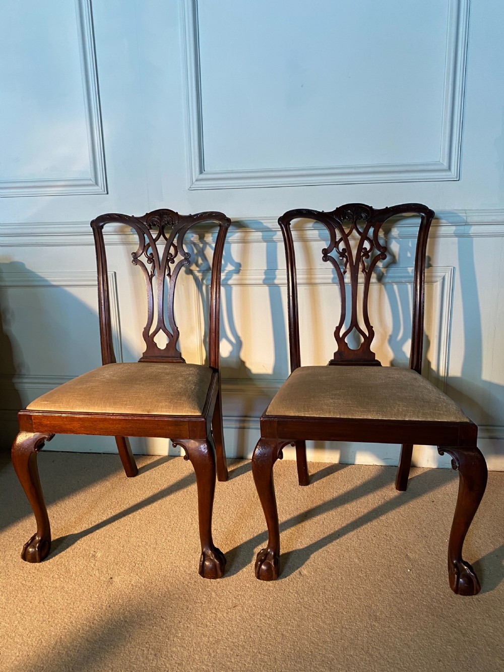 A pair of 19th-century Chippendale style dark mahogany dining chairs featuring carved pierced back splats, upholstered seats, and cabriole front legs ending in ball and claw feet. View II