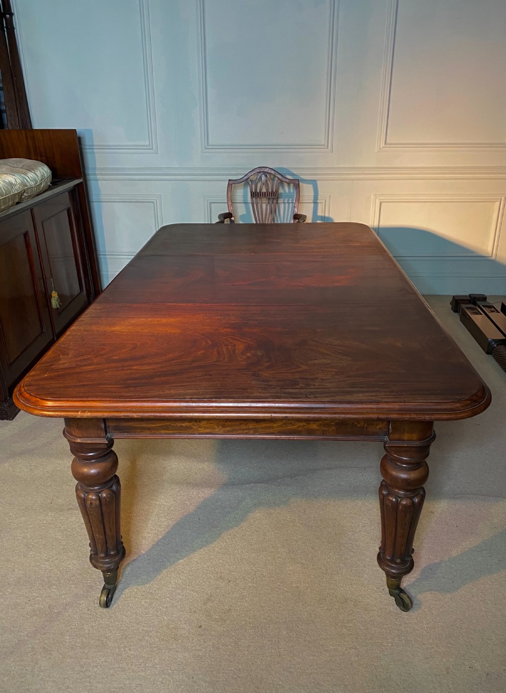 A 19th-century mahogany extending dining table featuring rounded corners, turned and reeded legs, and brass castors. View II