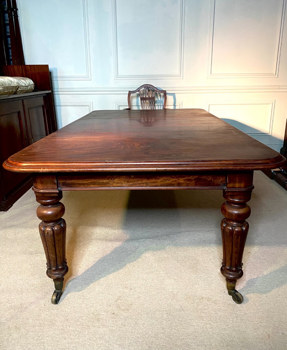 A 19th-century mahogany extending dining table featuring rounded corners, turned and reeded legs, and brass castors. View IX