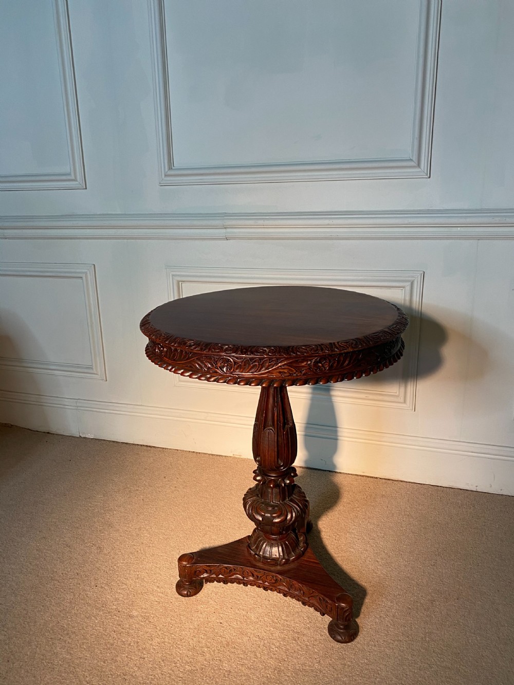 A circular Anglo-Indian padauk wood table featuring a heavily carved floral rim, turned central pedestal, and tripartite base. View II