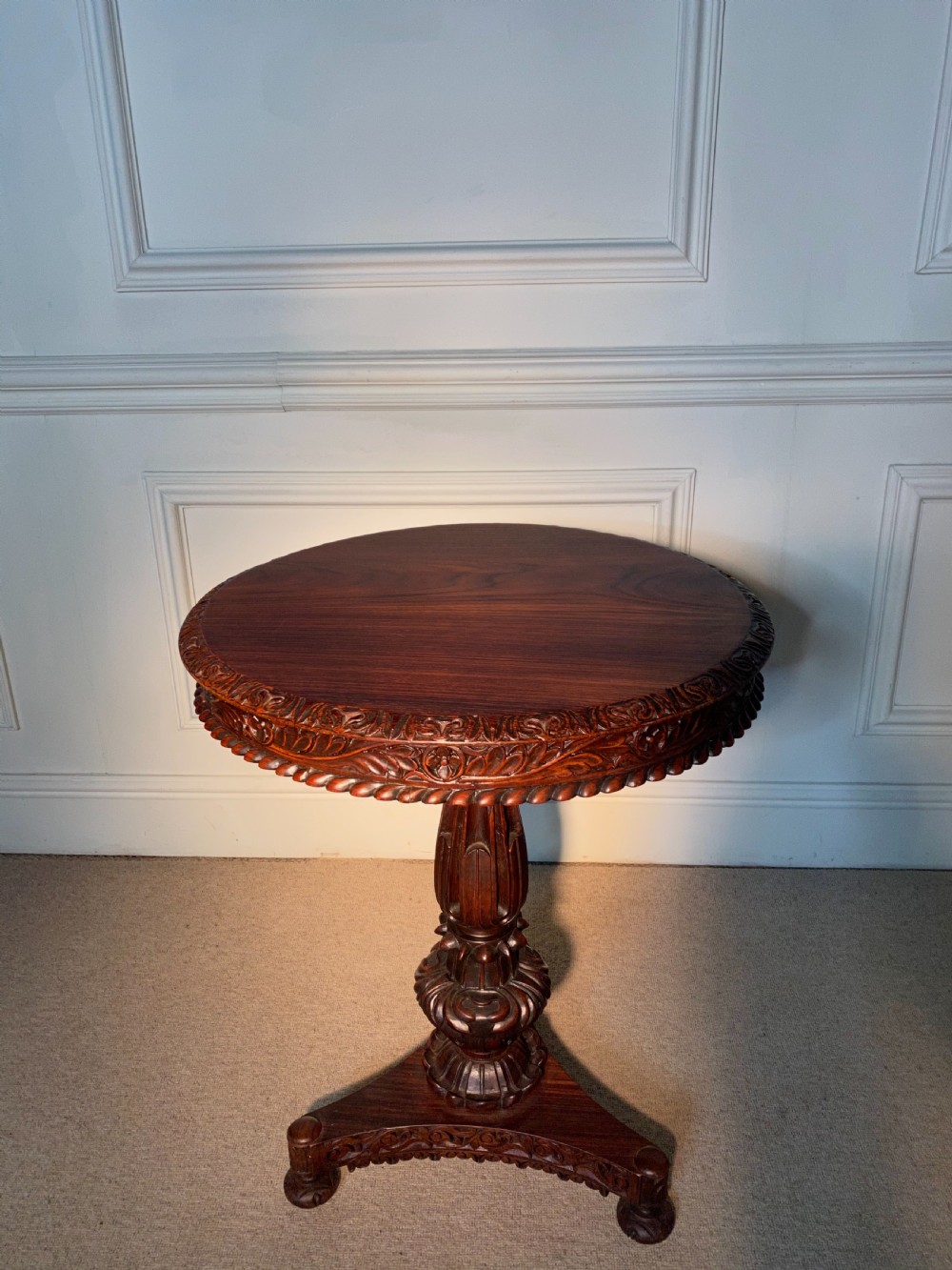 A circular Anglo-Indian padauk wood table featuring a heavily carved floral rim, turned central pedestal, and tripartite base. View III