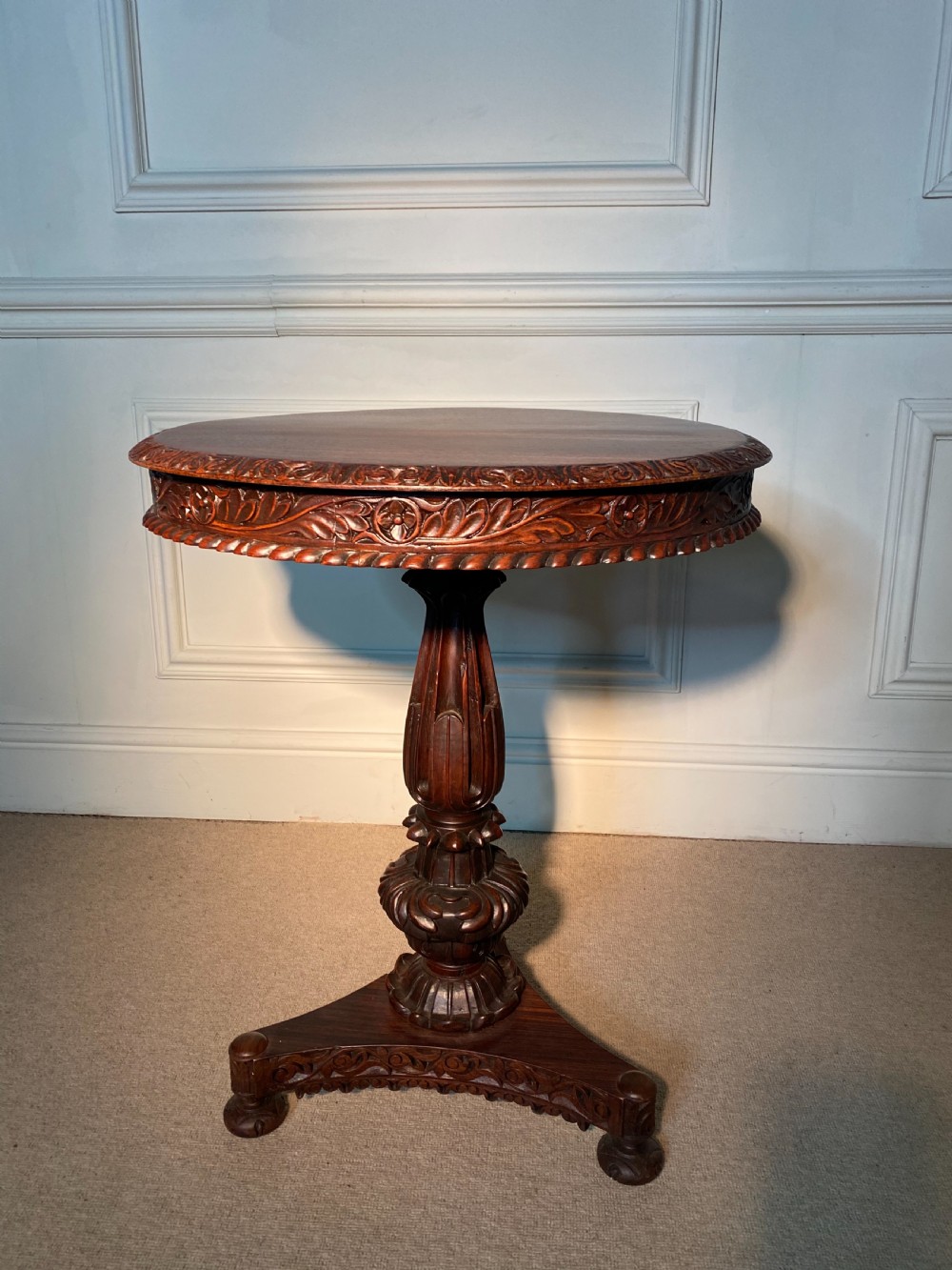 A circular Anglo-Indian padauk wood table featuring a heavily carved floral rim, turned central pedestal, and tripartite base. View IV