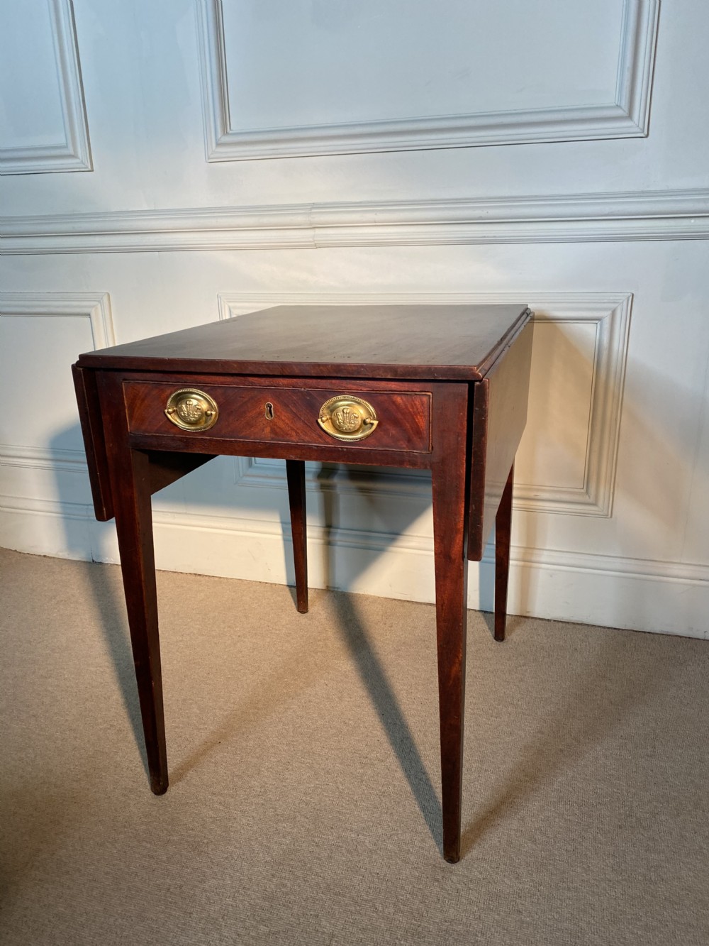 An 18th-century Chippendale mahogany Pembroke table with drop leaves, a single drawer featuring oval brass handles, and square tapered legs.