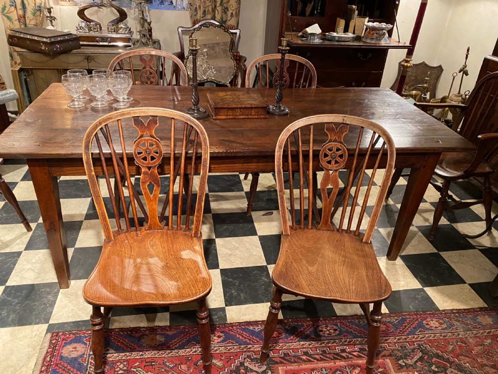 A set of antique wooden Windsor dining chairs featuring hoop backs, wheelback carved splats, spindle supports, shaped saddle seats, and turned legs.