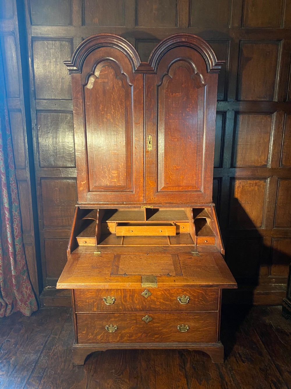 A George I period oak double-dome bureau cabinet featuring double arched panel doors above a sloping fall-front writing desk and graduated drawers with brass handles. View II