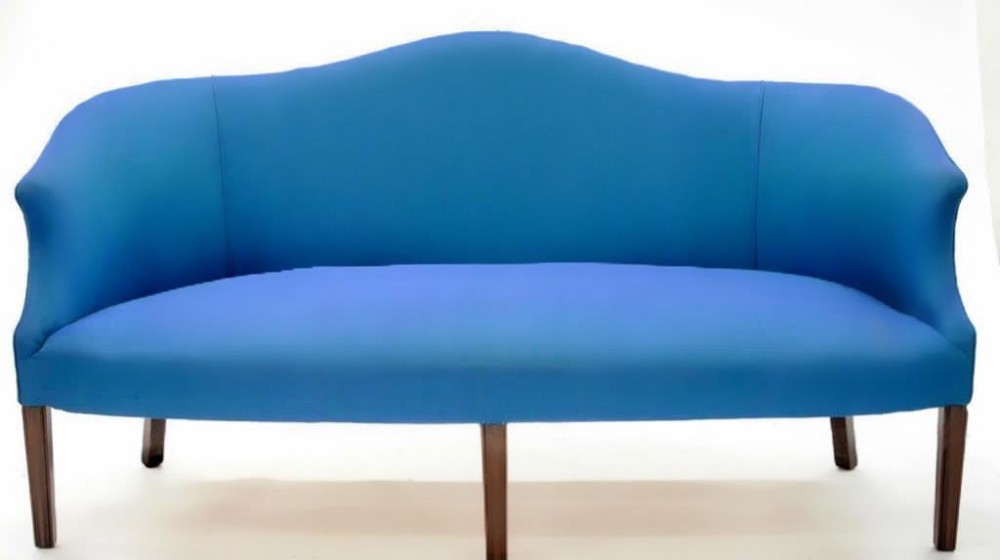 A Hepplewhite style camelback sofa upholstered in bright blue fabric featuring four tapered mahogany front legs and splayed rear legs.