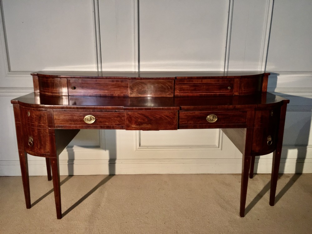 A George III mahogany sideboard featuring a stage top superstructure, boxwood inlay, brass ring handles, and square tapered legs.