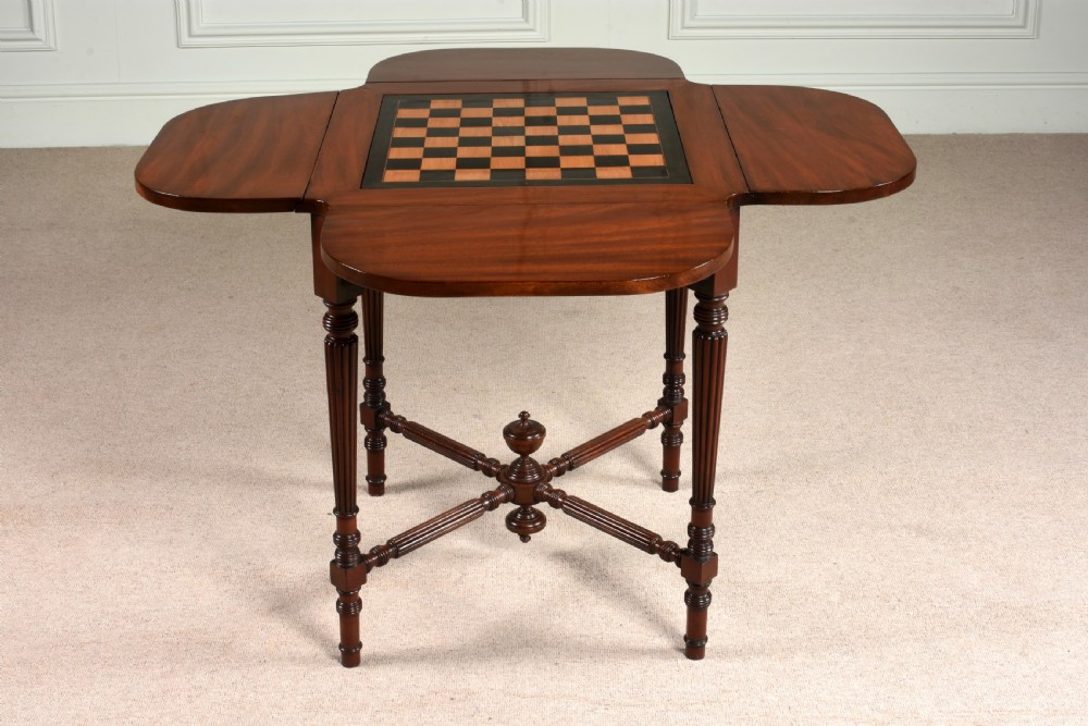 A 19th-century mahogany games table featuring a square top with an inlaid chessboard, two drop-leaf sides, reeded turned legs, and an X-stretcher with a central finial. View II