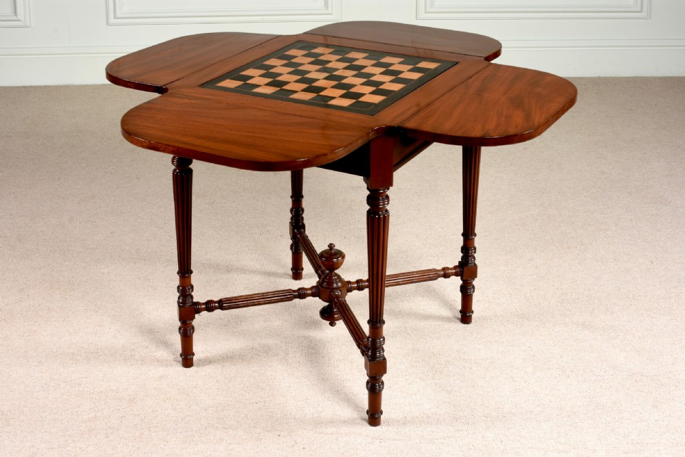 A 19th-century mahogany games table featuring a square top with an inlaid chessboard, two drop-leaf sides, reeded turned legs, and an X-stretcher with a central finial. View XI