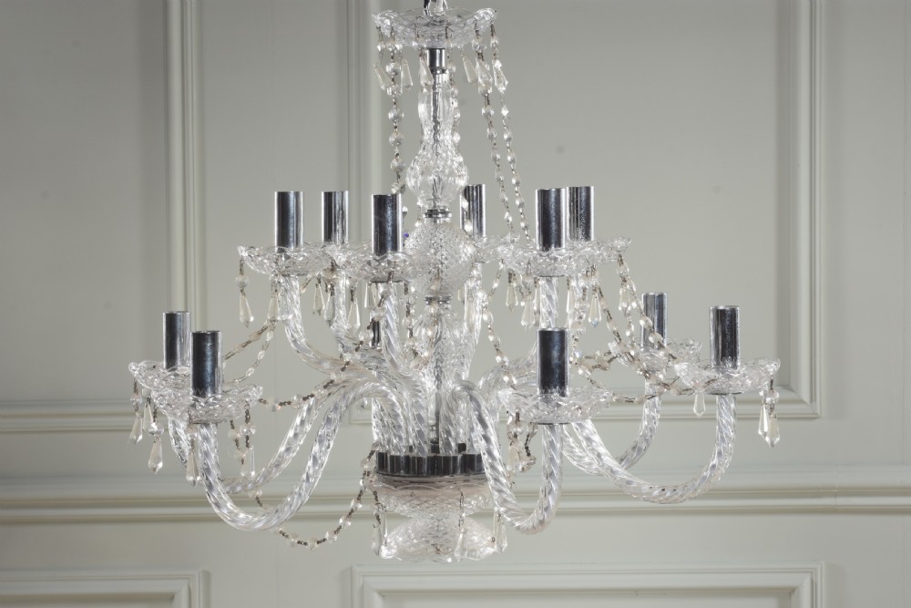 A twelve-light crystal chandelier featuring twisted glass arms, cut crystal drops, and central column detailing against a neutral wall.