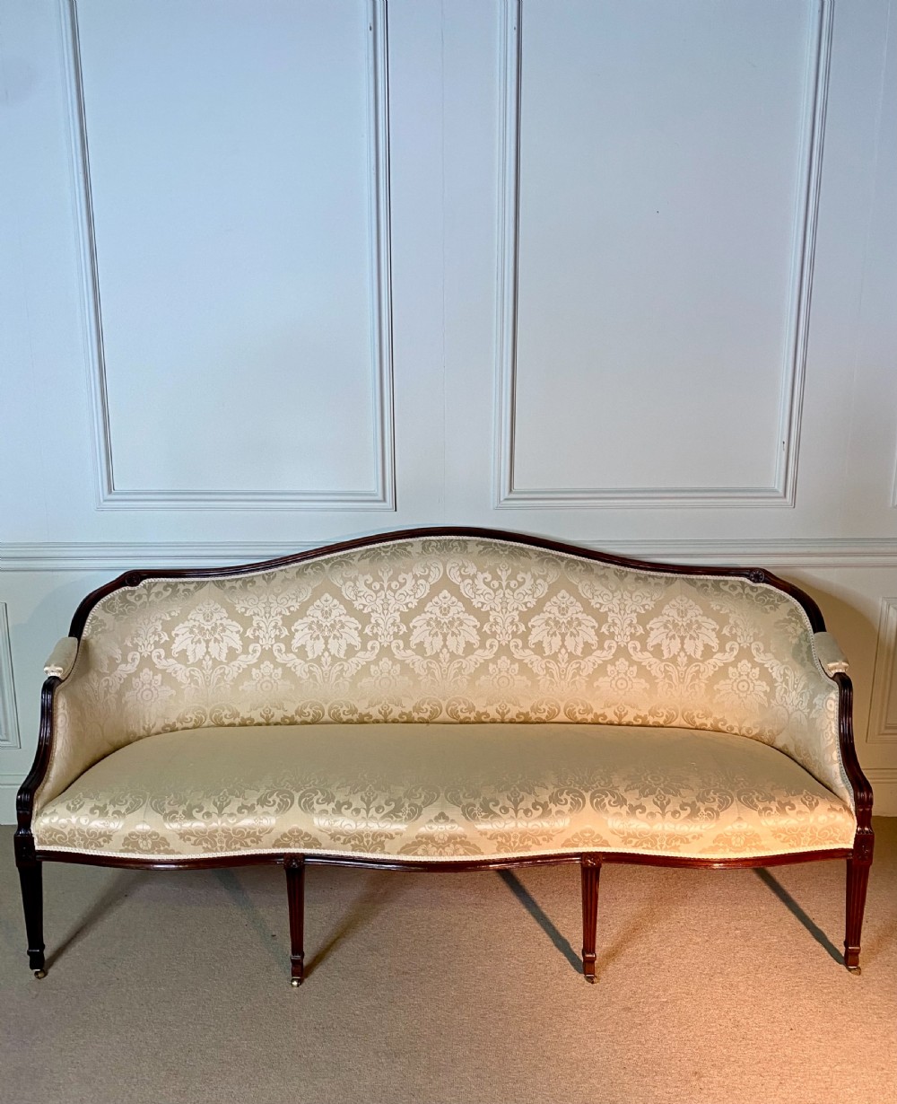 A George III Hepplewhite sofa featuring a serpentine back upholstered in cream damask fabric with dark mahogany reeded legs.