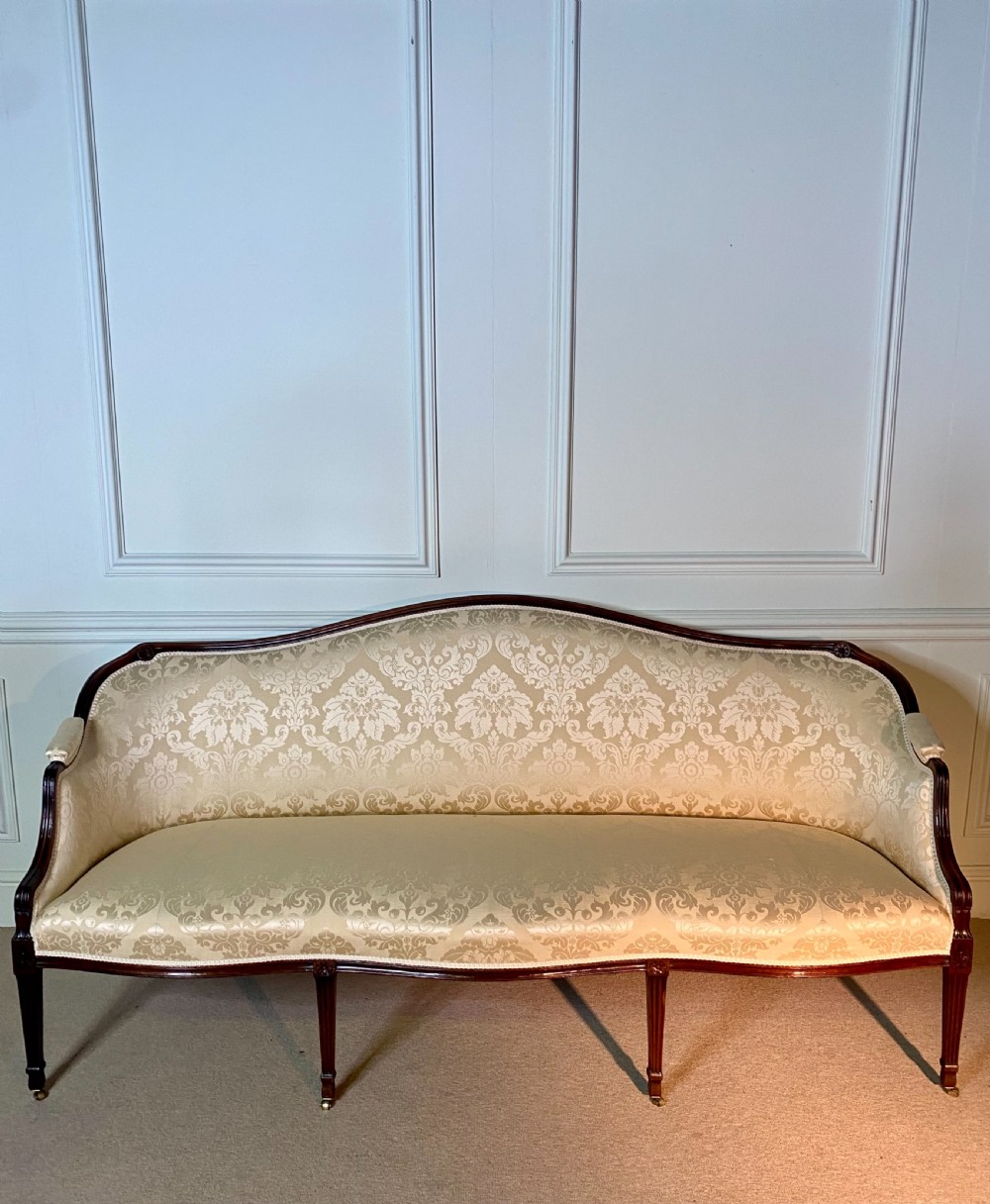 A George III Hepplewhite sofa featuring a serpentine back upholstered in cream damask fabric with dark mahogany reeded legs. View II