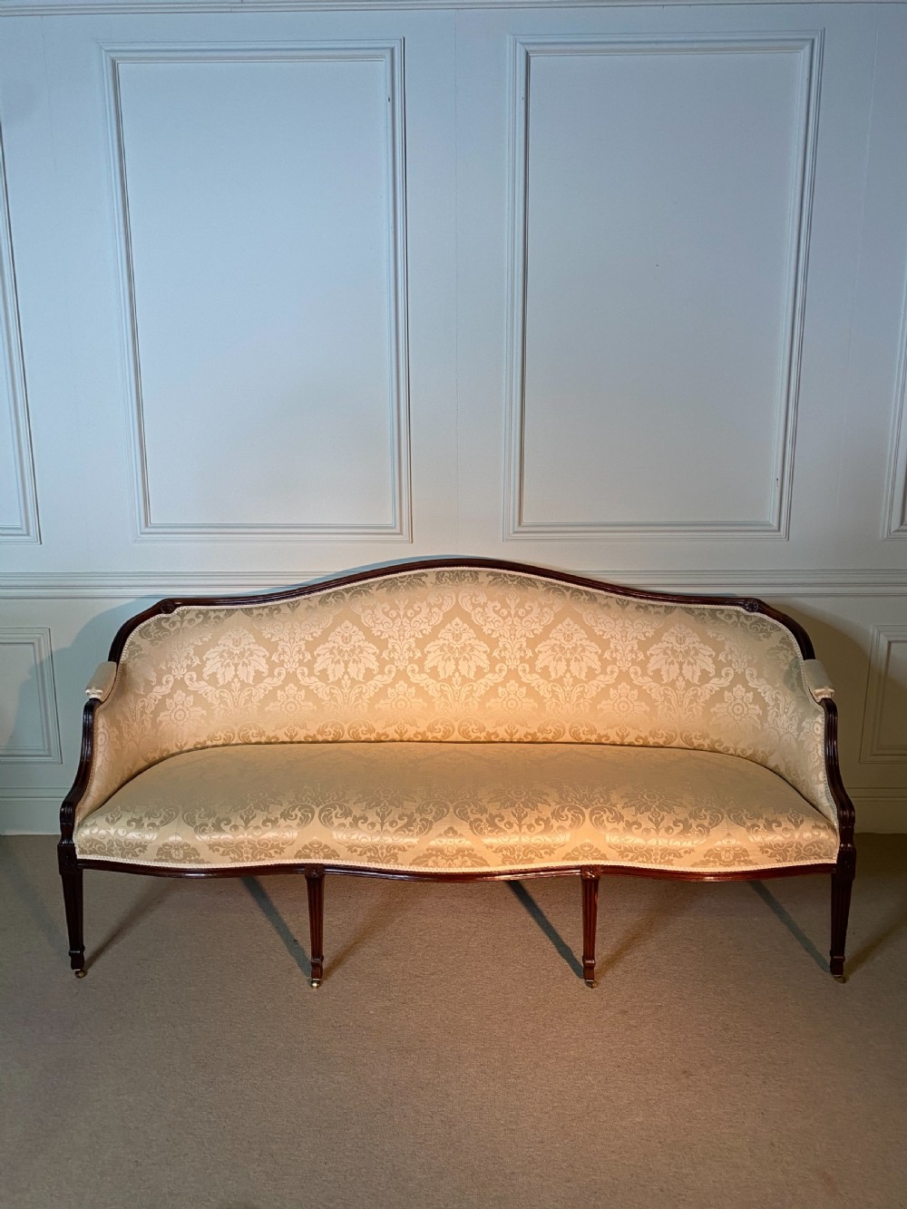 A George III Hepplewhite sofa featuring a serpentine back upholstered in cream damask fabric with dark mahogany reeded legs. View III
