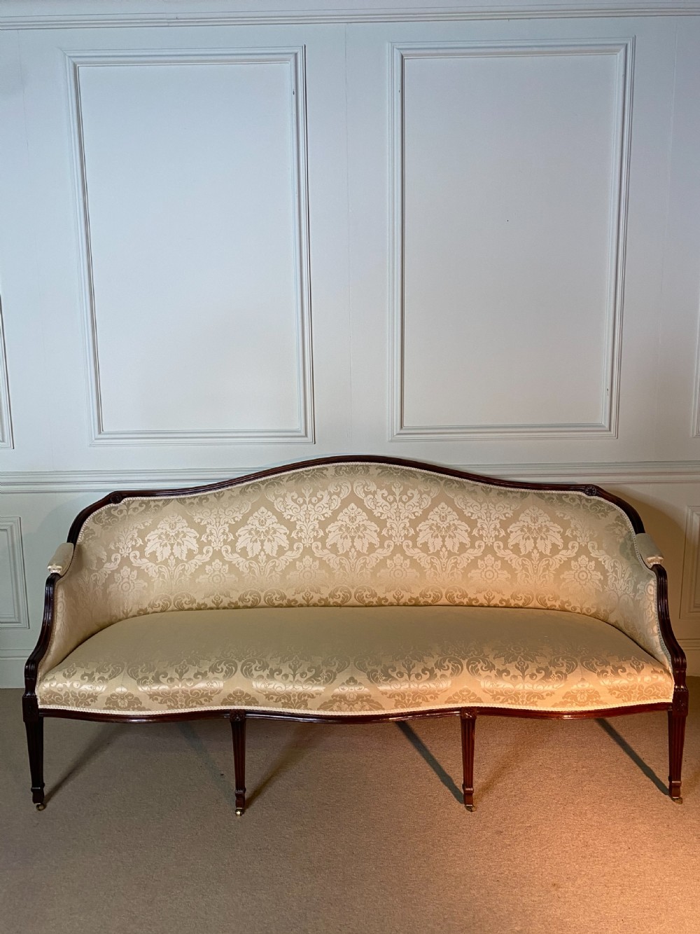 A George III Hepplewhite sofa featuring a serpentine back upholstered in cream damask fabric with dark mahogany reeded legs. View VII