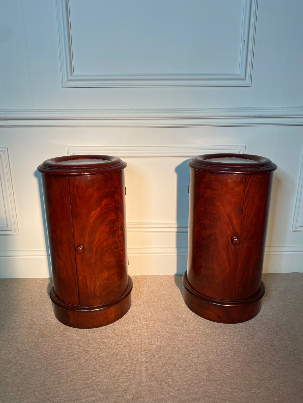 A pair of 19th-century cylindrical flame mahogany bedside cupboards featuring inset marble tops and single curved doors with turned wooden knobs.