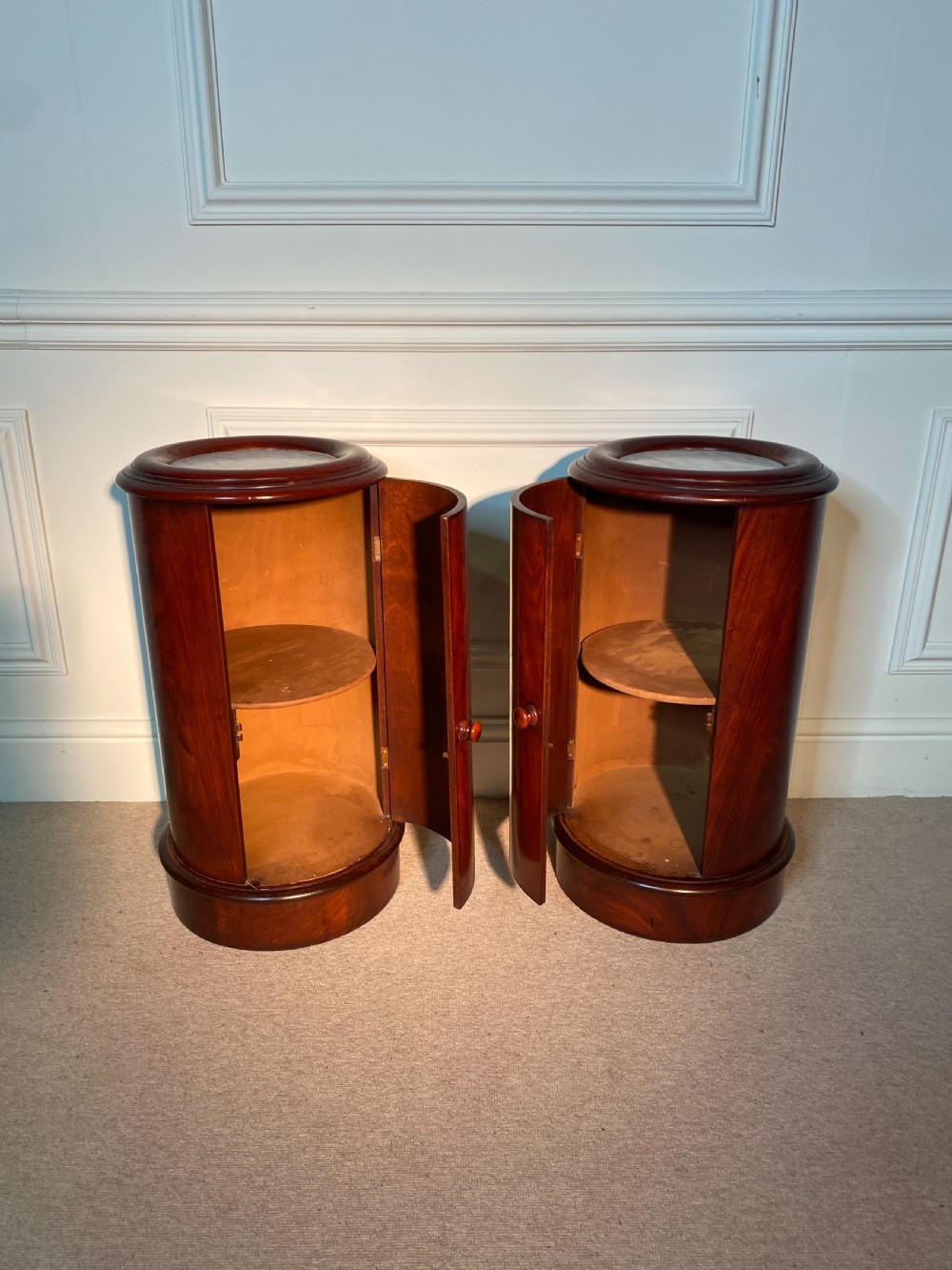 A pair of 19th-century cylindrical flame mahogany bedside cupboards featuring inset marble tops and single curved doors with turned wooden knobs. View II