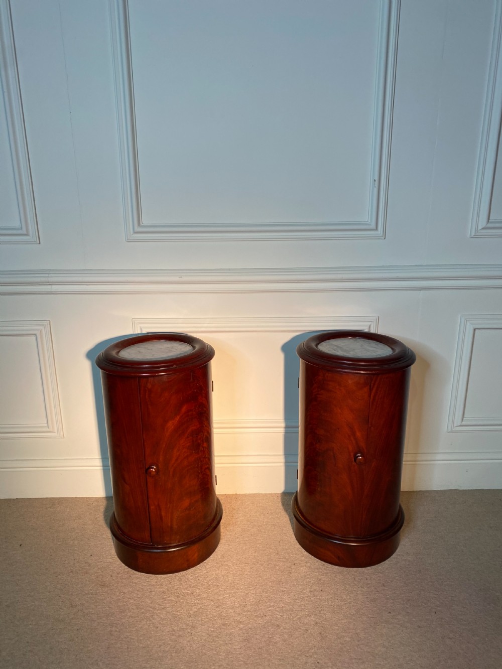 A pair of 19th-century cylindrical flame mahogany bedside cupboards featuring inset marble tops and single curved doors with turned wooden knobs. View III