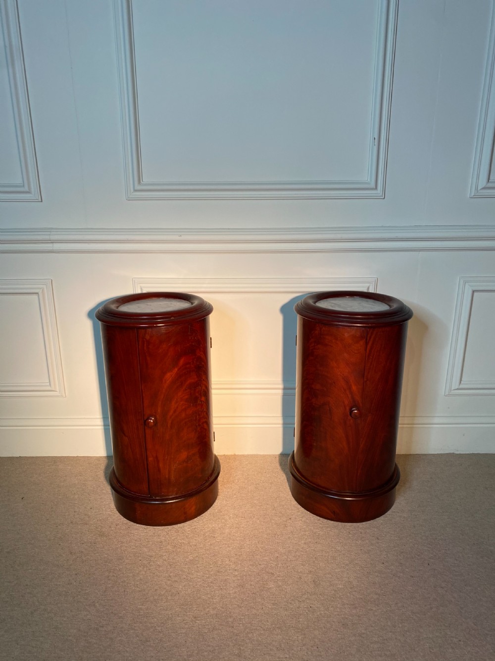 A pair of 19th-century cylindrical flame mahogany bedside cupboards featuring inset marble tops and single curved doors with turned wooden knobs. View V