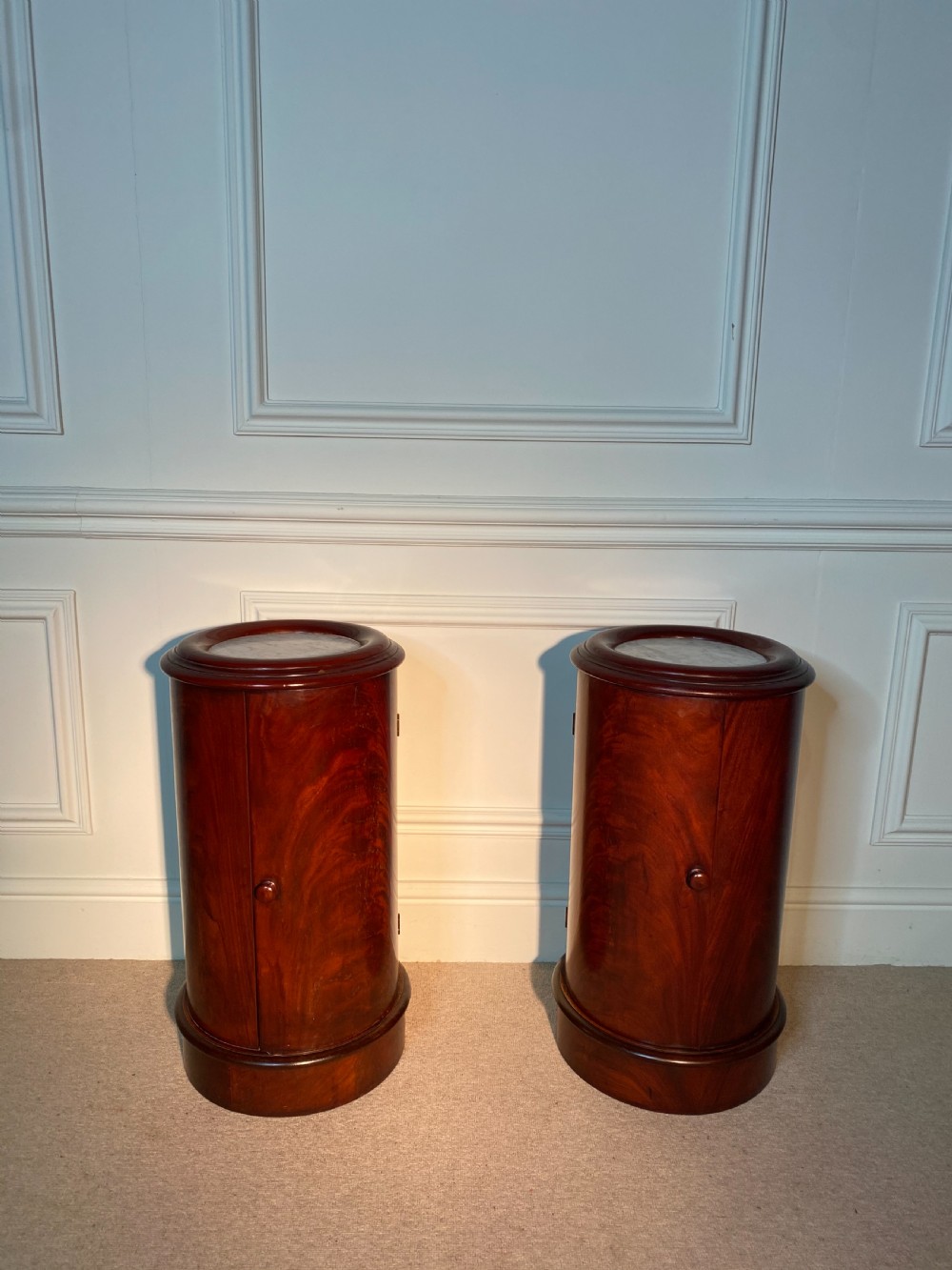 A pair of 19th-century cylindrical flame mahogany bedside cupboards featuring inset marble tops and single curved doors with turned wooden knobs. View VII