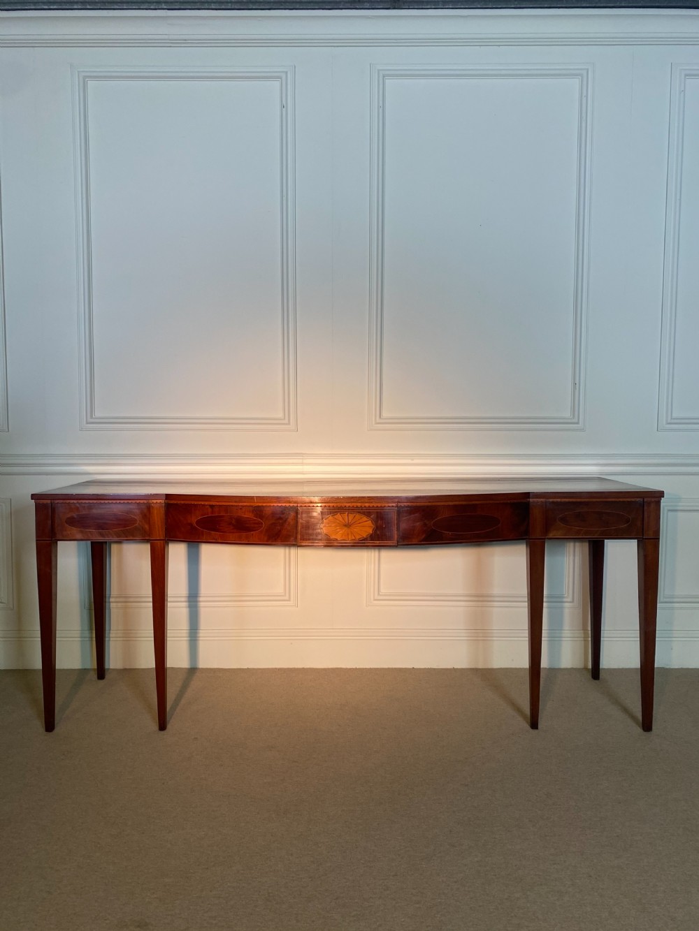 A George III mahogany bow-fronted serving table featuring inlaid oval panels, a central fan patera motif, and tapered square legs.