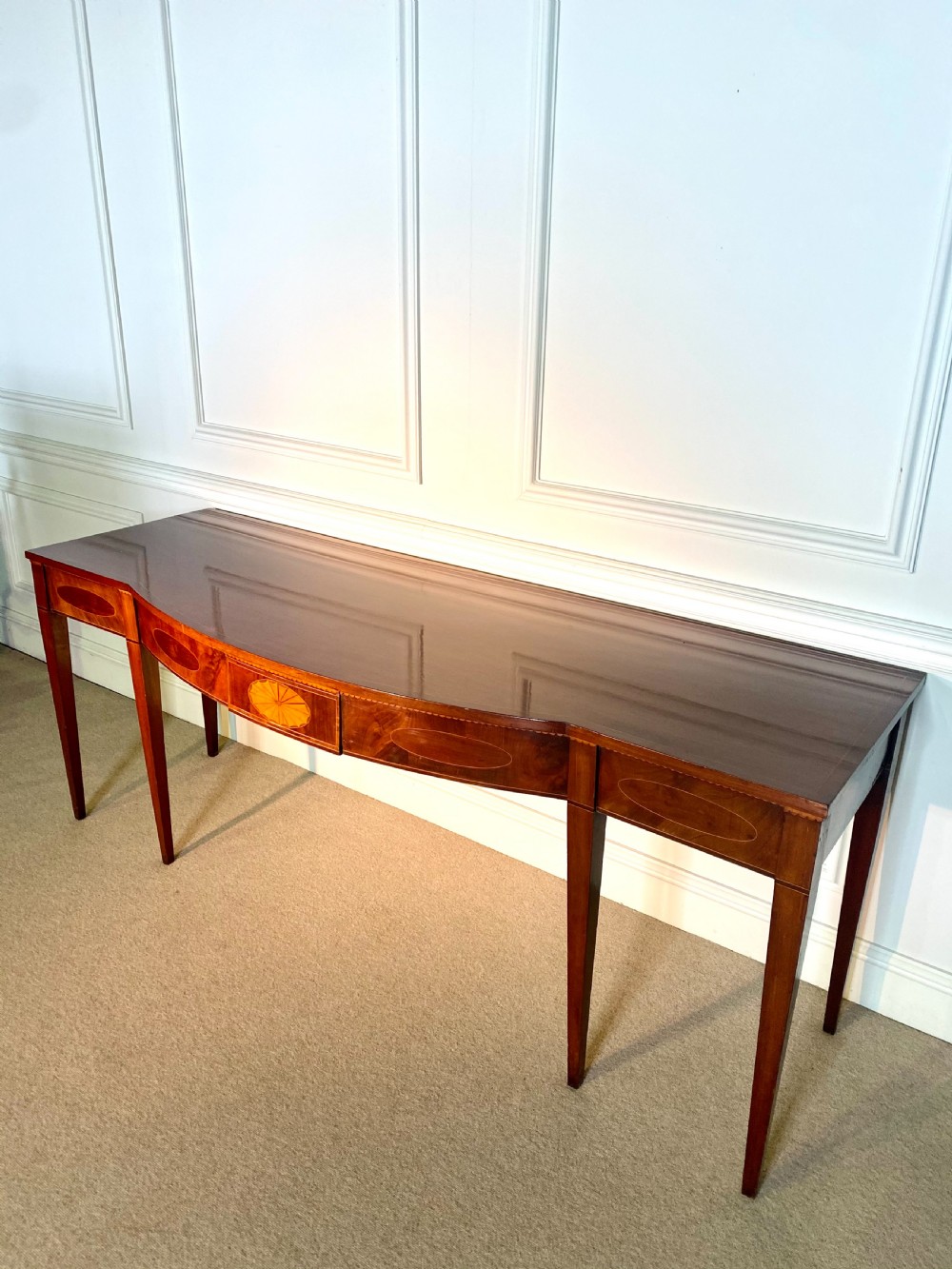 A George III mahogany bow-fronted serving table featuring inlaid oval panels, a central fan patera motif, and tapered square legs. View II