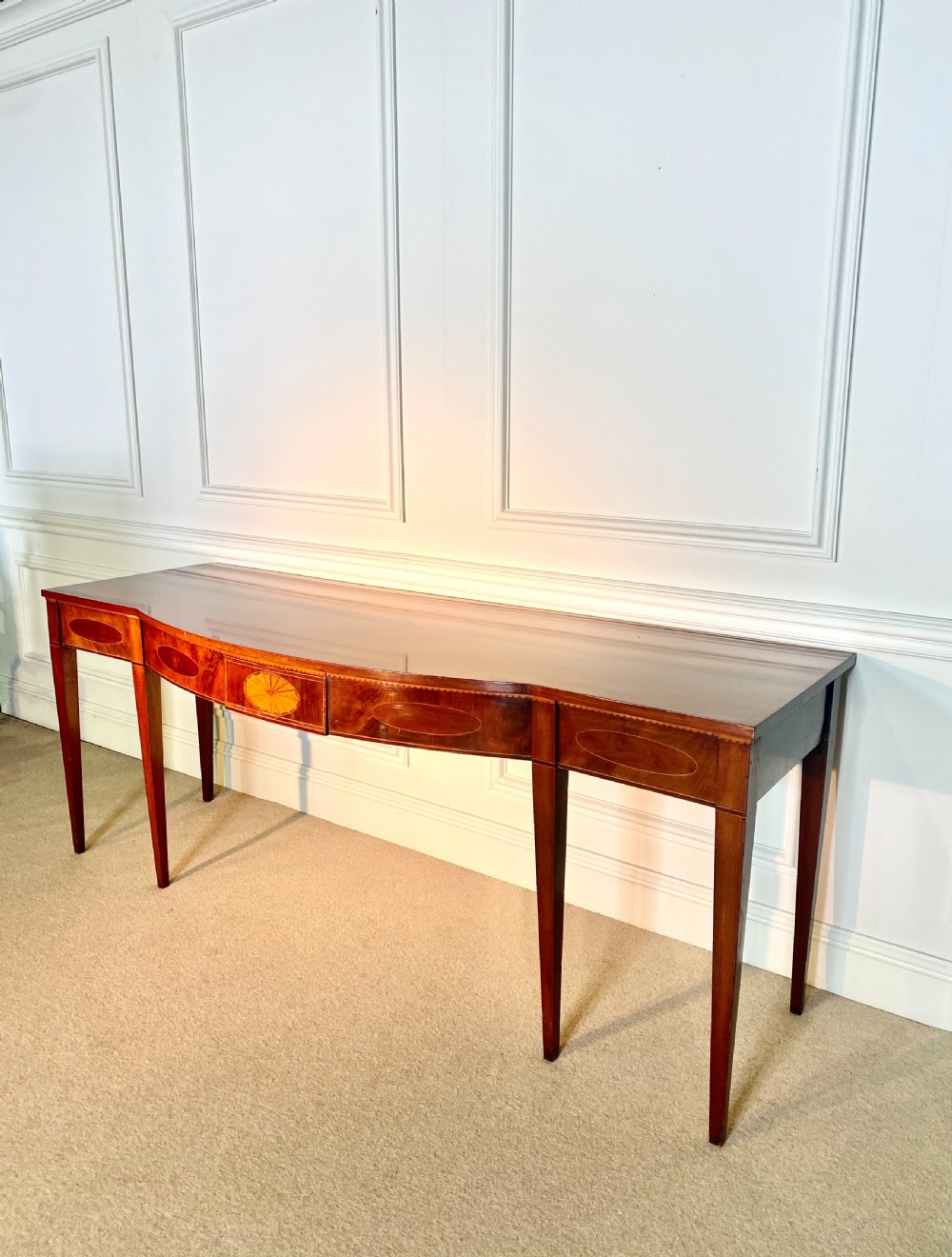 A George III mahogany bow-fronted serving table featuring inlaid oval panels, a central fan patera motif, and tapered square legs. View III