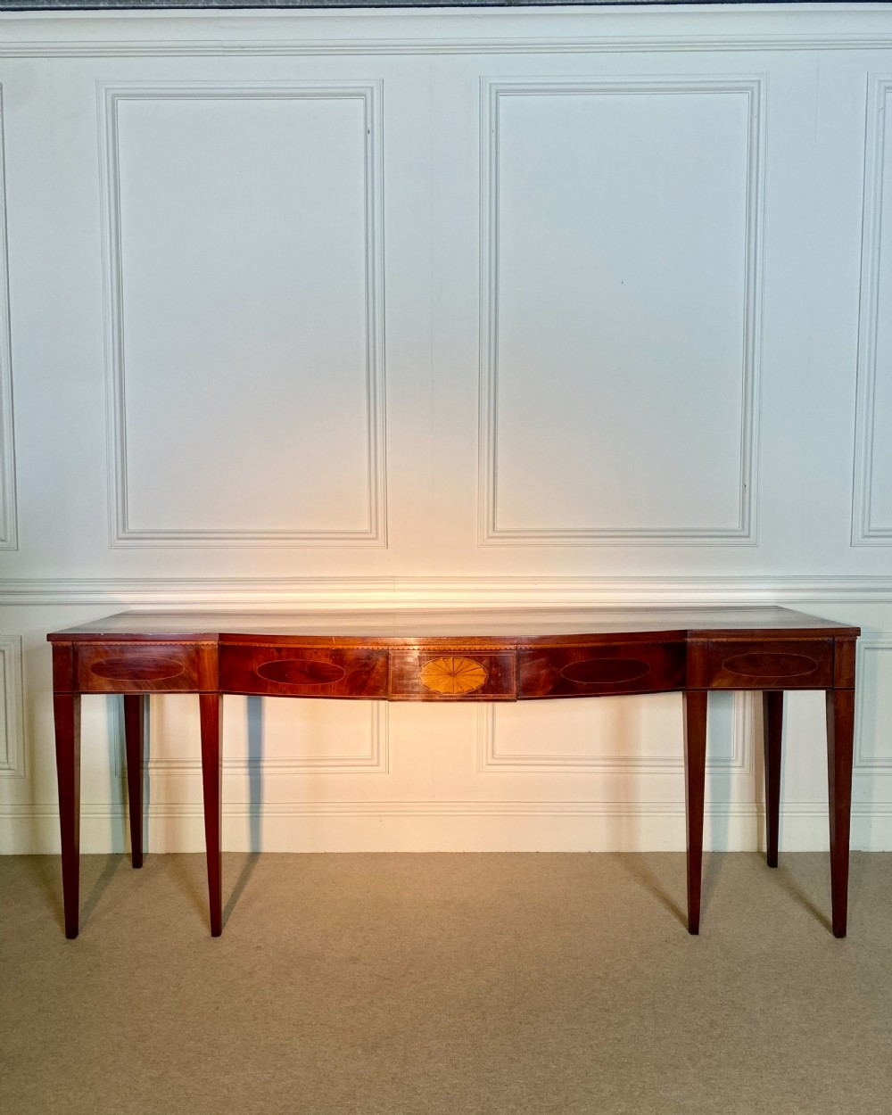 A George III mahogany bow-fronted serving table featuring inlaid oval panels, a central fan patera motif, and tapered square legs. View V