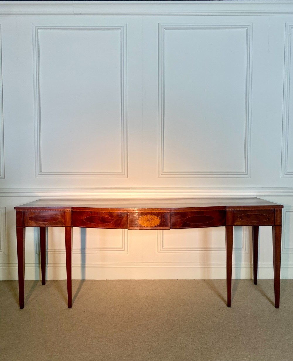 A George III mahogany bow-fronted serving table featuring inlaid oval panels, a central fan patera motif, and tapered square legs. View VI