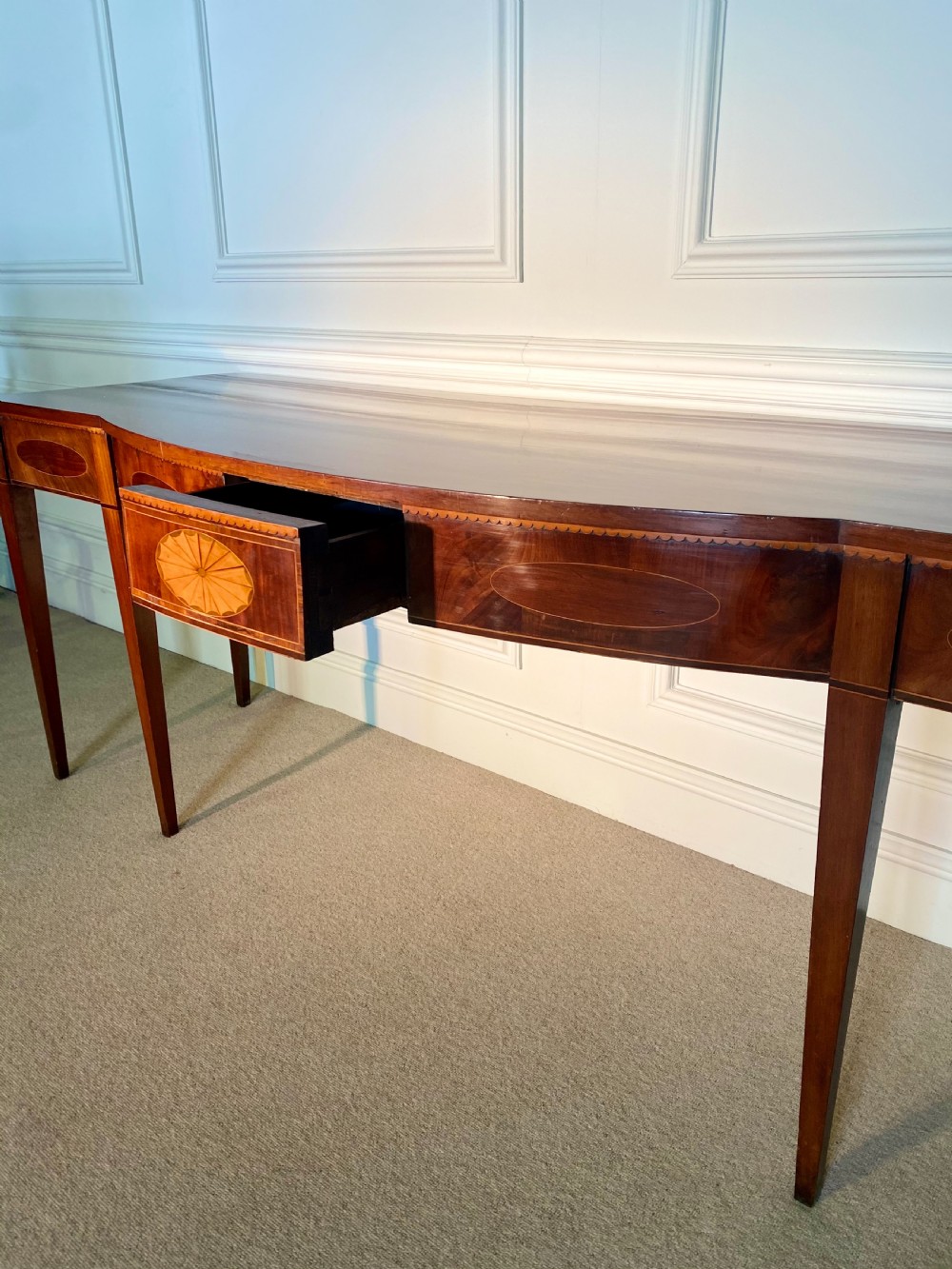 A George III mahogany bow-fronted serving table featuring inlaid oval panels, a central fan patera motif, and tapered square legs. View VII