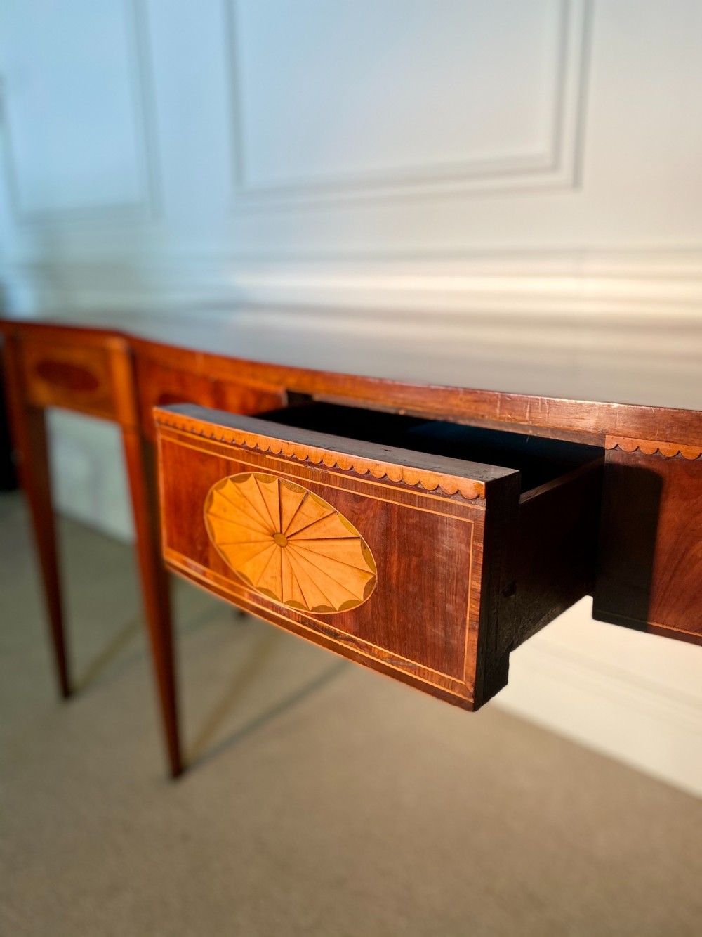 A George III mahogany bow-fronted serving table featuring inlaid oval panels, a central fan patera motif, and tapered square legs. View VIII