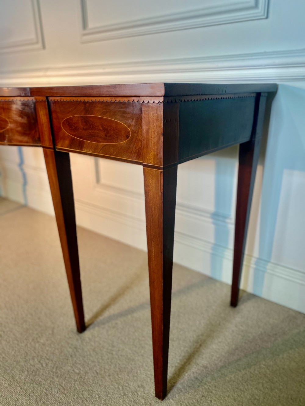 A George III mahogany bow-fronted serving table featuring inlaid oval panels, a central fan patera motif, and tapered square legs. View IX