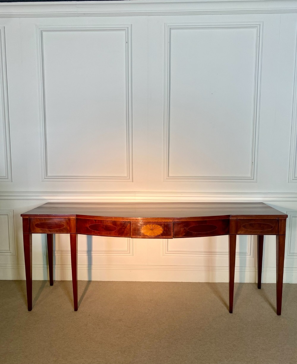 A George III mahogany bow-fronted serving table featuring inlaid oval panels, a central fan patera motif, and tapered square legs. View X