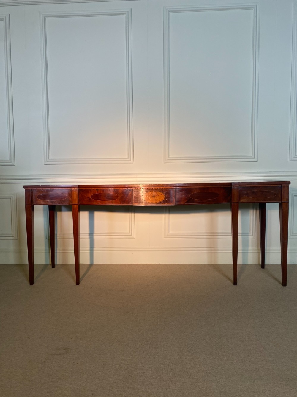 A George III mahogany bow-fronted serving table featuring inlaid oval panels, a central fan patera motif, and tapered square legs. View XI