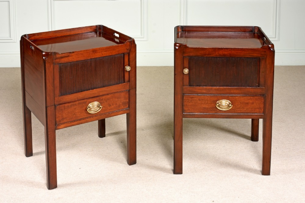 A pair of 18th-century George III mahogany bedside commodes featuring tray tops with handles, tambour shutter doors, and brass drawer handles.
