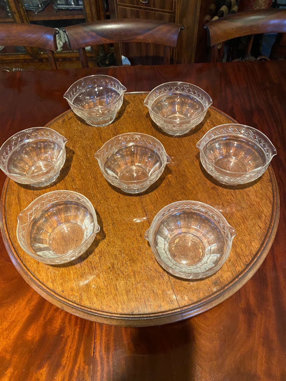 A set of seven 19th-century clear cut crystal finger bowls with diamond-patterned borders and small lip spouts.