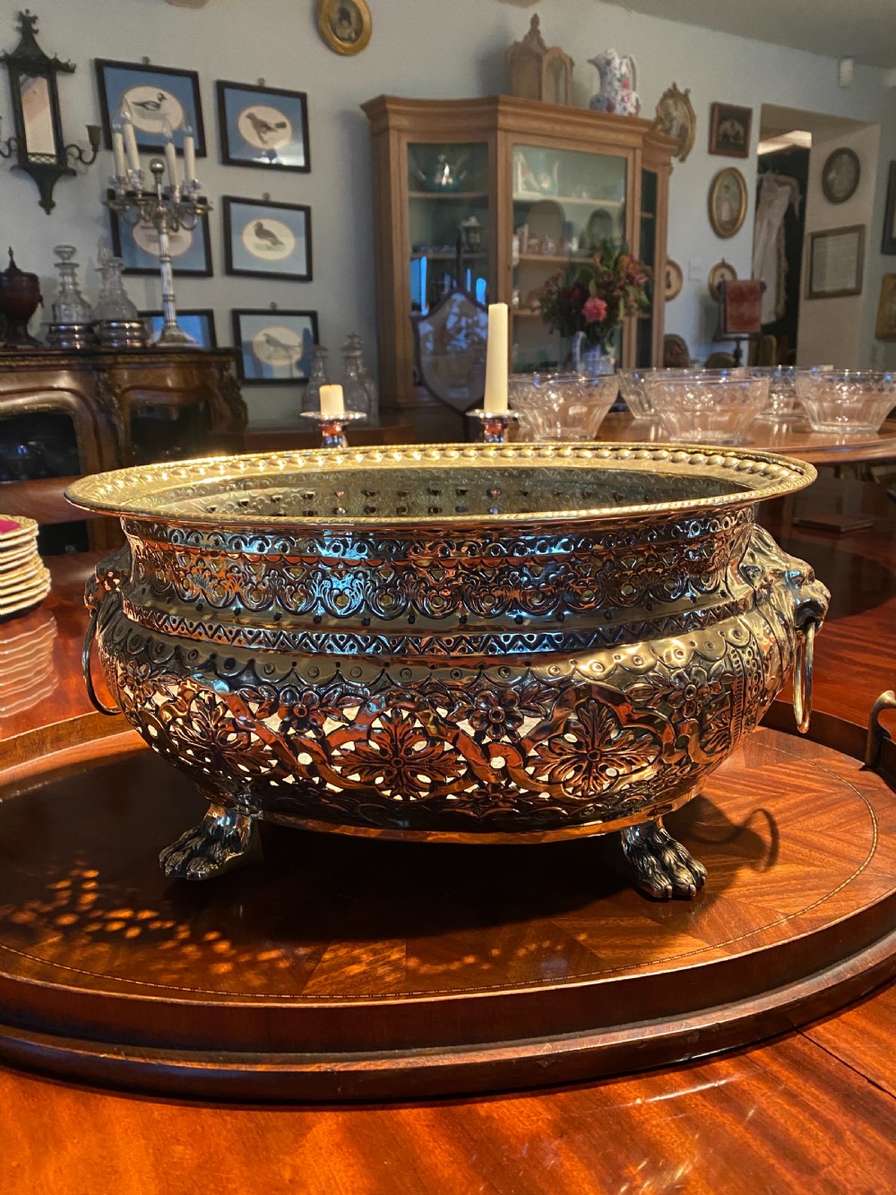 An oval polished brass wine cooler featuring intricate pierced repousse detailing, side lion mask handles with ring pulls, and four claw feet. View II
