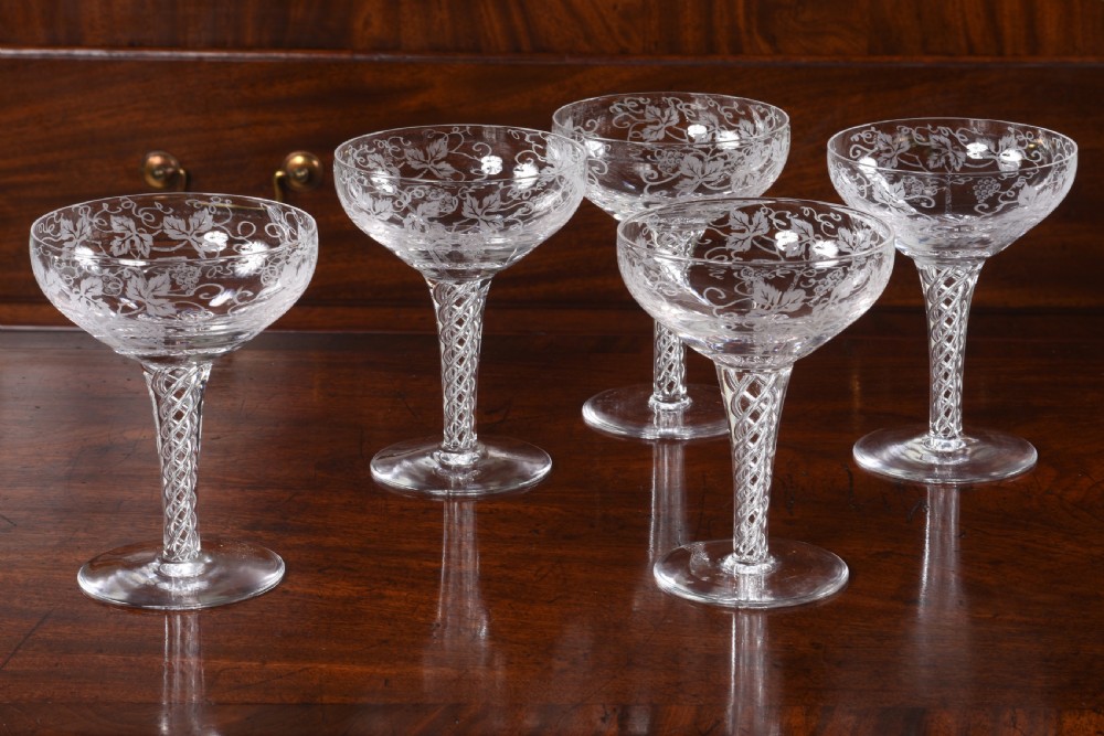 A set of sixteen clear etched crystal champagne coupes with diamond patterned rims displayed on a dark wood surface. View V