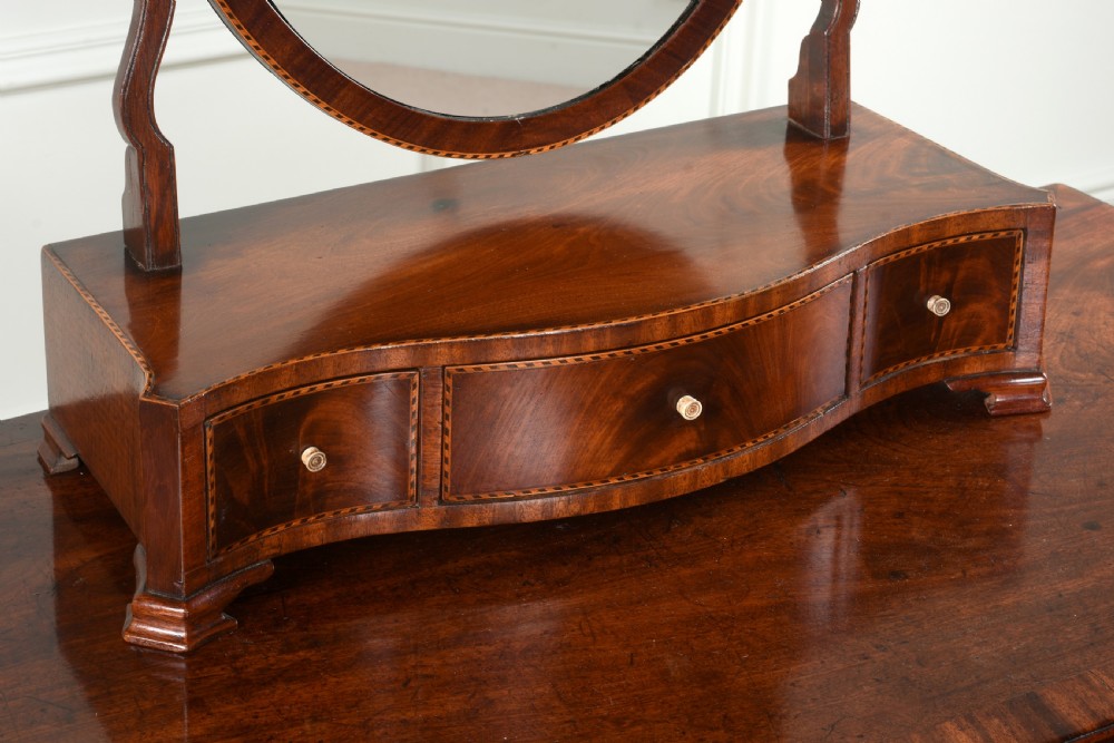 An antique George III mahogany dressing table mirror featuring an oval swing glass on curved supports above a serpentine base with three inlaid drawers. View II