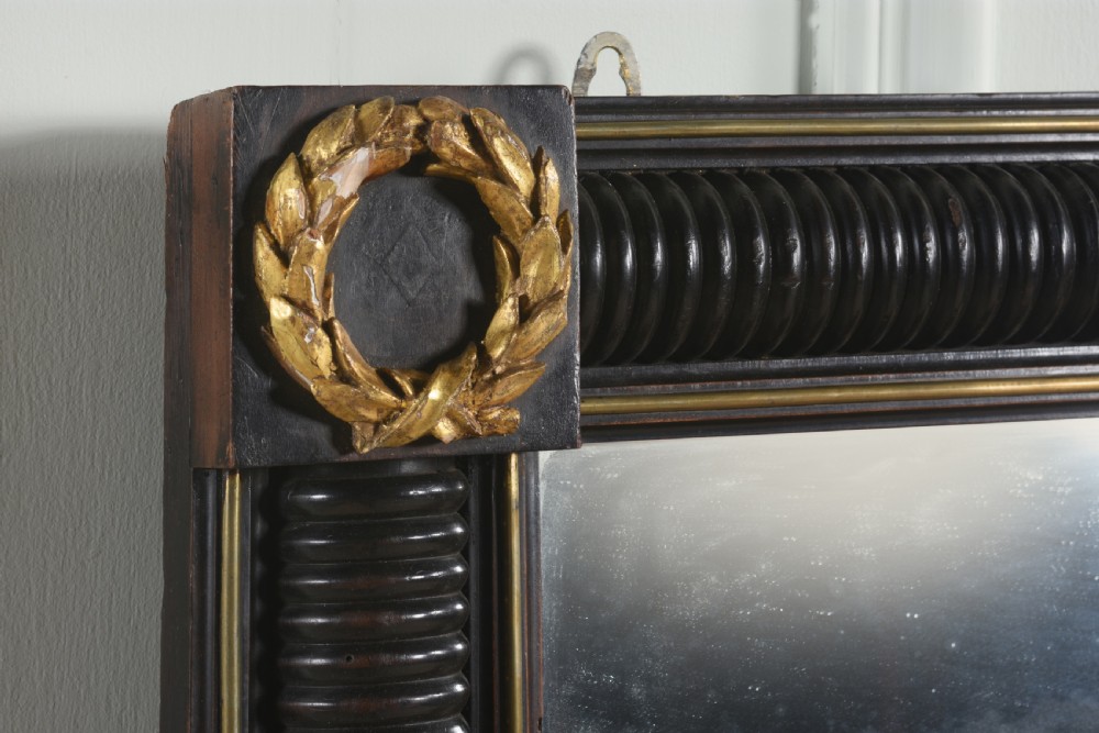 A rectangular Regency overmantel mirror featuring an ebonised reeded frame with gold laurel wreath corner ornaments and a central gilded greyhound motif at the top. View II