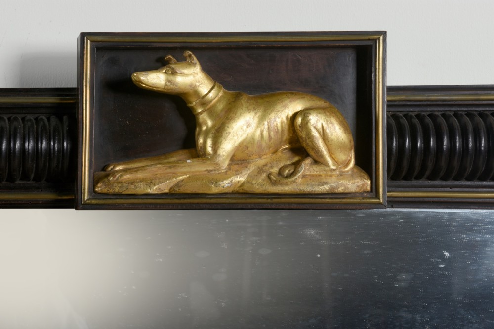 A rectangular Regency overmantel mirror featuring an ebonised reeded frame with gold laurel wreath corner ornaments and a central gilded greyhound motif at the top. View III