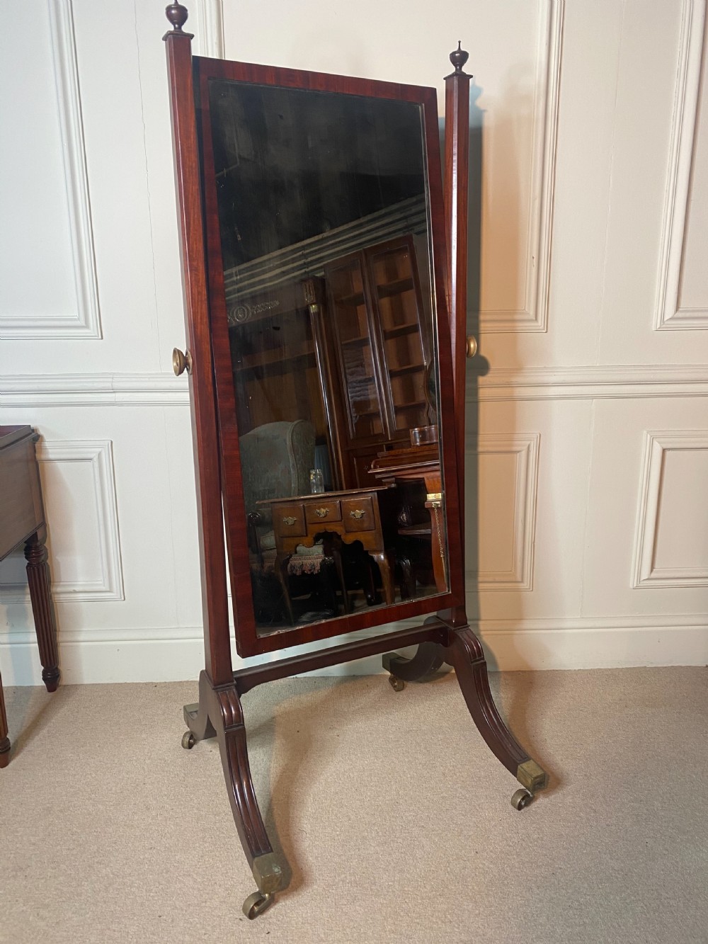 A Regency mahogany cheval mirror featuring a rectangular tilting plate supported by vertical columns with finials and splayed reeded legs on brass castors.