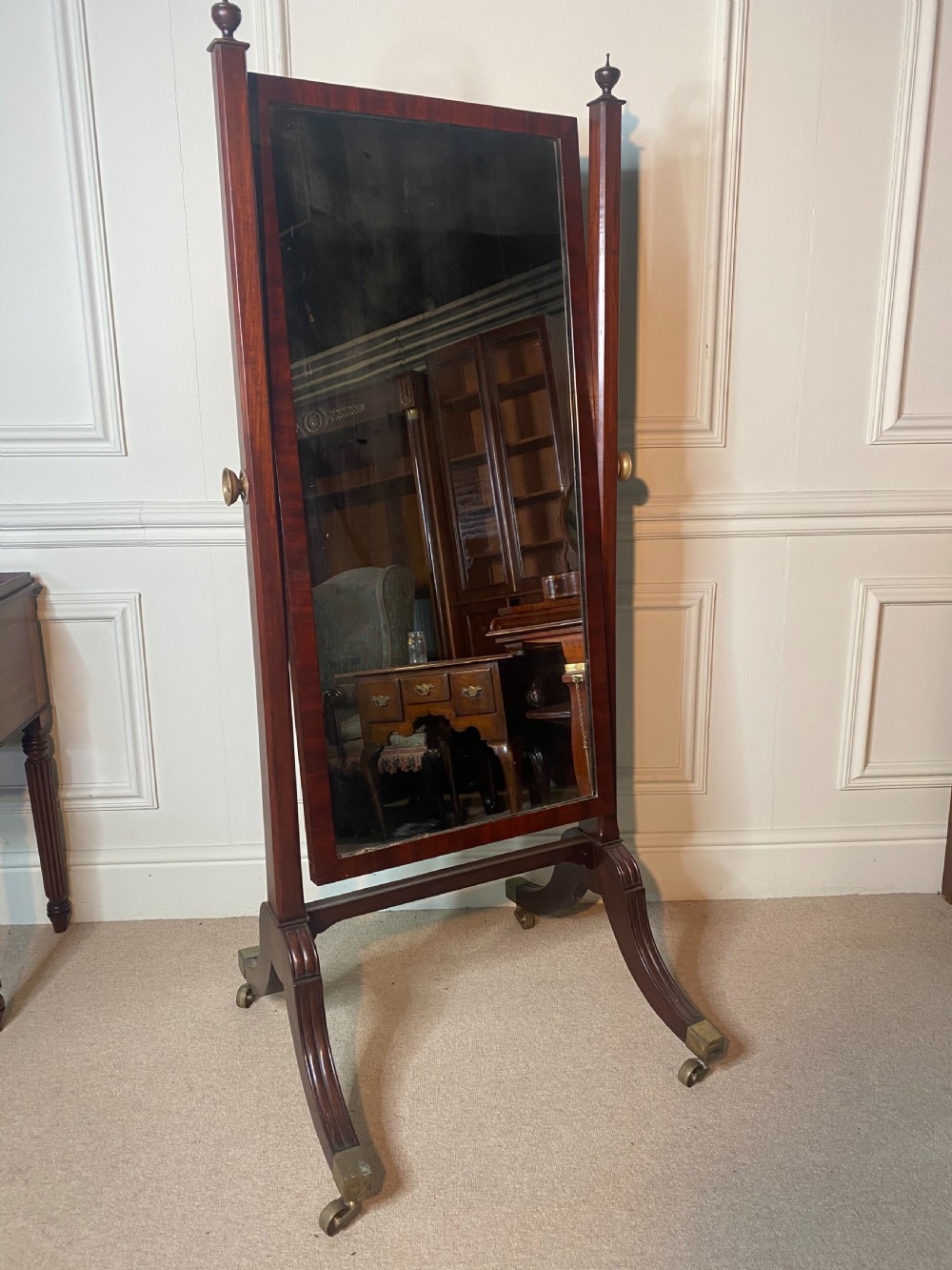 A Regency mahogany cheval mirror featuring a rectangular tilting plate supported by vertical columns with finials and splayed reeded legs on brass castors. View II