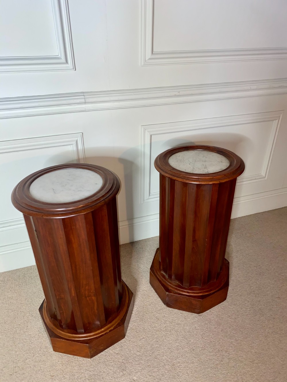 A pair of cylindrical mahogany bedside stands featuring fluted wooden columns, inset marble tops, and octagonal plinth bases. View V