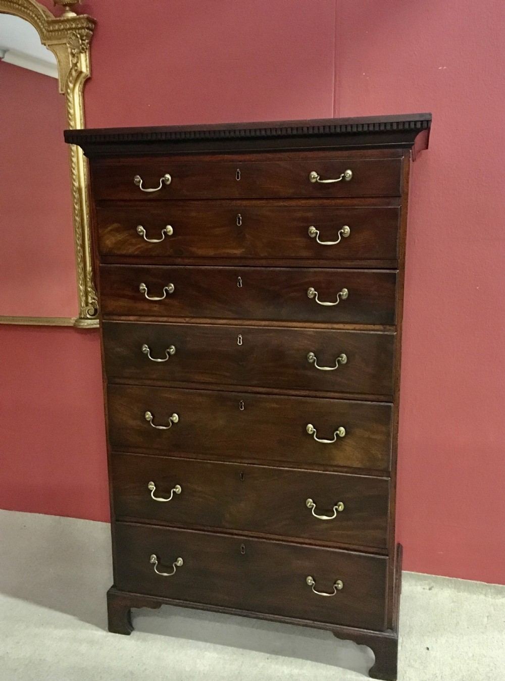 A tall George III mahogany secretaire tallboy featuring seven graduated drawers, brass swan-neck handles, dentil moulding, and bracket feet.